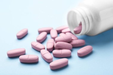 Açık mavi arka planda vitamin hapları ve şişe, yakın plan.
