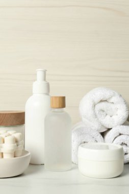 Farklı banyo aksesuarları ve kişisel bakım ürünleri beyaz masada, tahta duvarın yanında.