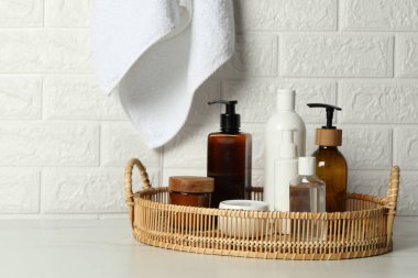 Farklı banyo aksesuarları ve kişisel bakım ürünleri tuğla duvarın yanındaki beyaz masada.