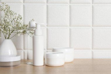 Banyo aksesuarları. Farklı kişisel bakım ürünleri ve vazodaki çingene çiçekleri beyaz kiremitli duvarın yanındaki ahşap masada, metin için yer var.