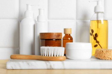 Farklı banyo aksesuarları ve beyaz kiremitli duvarın yanındaki ahşap masada kişisel bakım ürünleri.