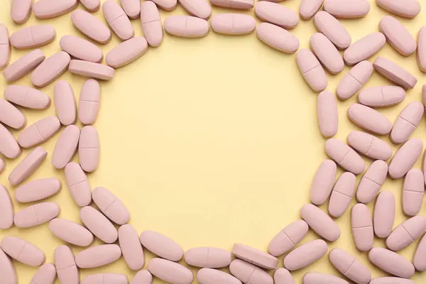 Frame made of vitamin pills on pale yellow background, top view. Space for text