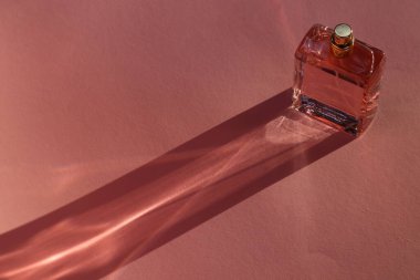 Lüks kadın parfümü. Soluk pembe arka planda güneş ışığı şişesi. Metin için boşluk