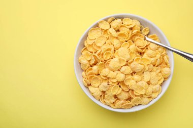 Kahvaltı gevreği. Lezzetli mısır gevrekleri kasede ve kaşık sarı masada, üst manzara. Metin için boşluk