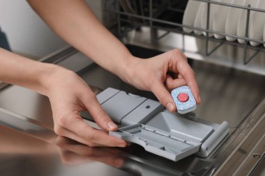 Kadın bulaşık makinesine deterjan koyuyor, yakın plan.