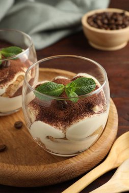 Bardakta nefis tiramisu, nane yaprakları, kahve çekirdekleri ve kaşıklar ahşap masada, yakın plan.