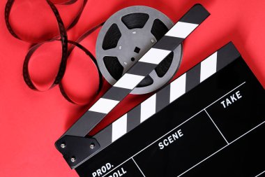 Kırmızı arkaplanda el çırpma tahtası ve film makarası, üst görünüm