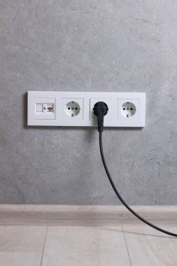 Gri duvarda elektrik prizi ve prizler var.
