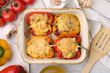 Pişirme kabında dolma biber, spatula ve beyaz desenli masa üzerindeki malzemeler düz.