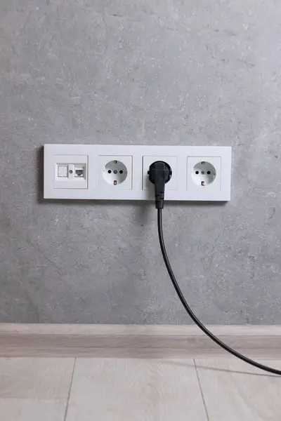 Power sockets and electric plug on grey wall
