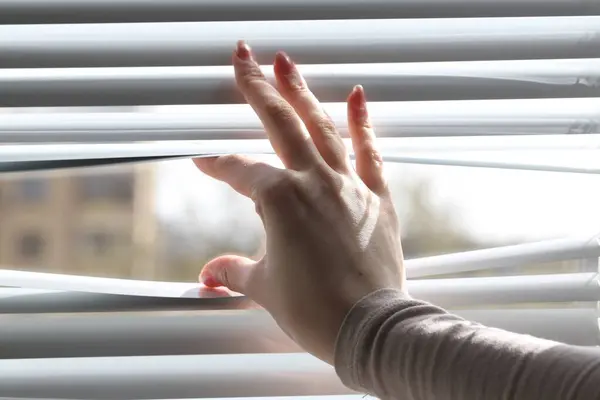 stock image Woman separating slats of white blinds indoors, closeup