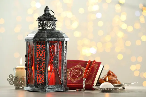 stock image Arabic lantern, Quran, misbaha, candles and dates on table against blurred lights