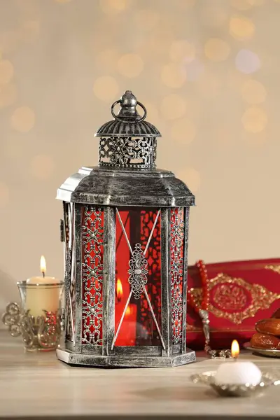 stock image Arabic lantern, Quran, misbaha and candles on wooden table against blurred lights