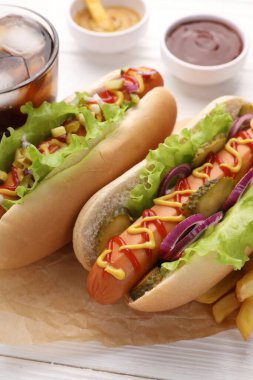 Marul, soğan ve turşulu lezzetli sosisliler beyaz ahşap masada, yakın plan.