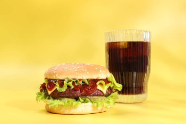 Lezzetli köfteli hamburger ve sarı arka planda soda.