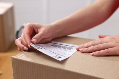 Paketleme. Postane çalışanı kapalı bir kutuya barkod yapıştırıyor.