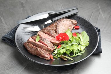 Gri masadaki yeşilliklerle servis edilen lezzetli ızgara et.