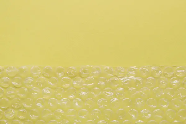 Transparent bubble wrap on yellow background, top view. Space for text