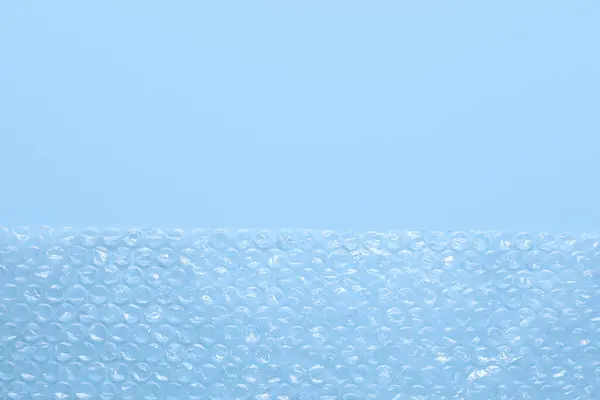 Transparent bubble wrap on light blue background, top view. Space for text