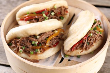 Delicious gua bao in bamboo steamer on wooden table, closeup clipart