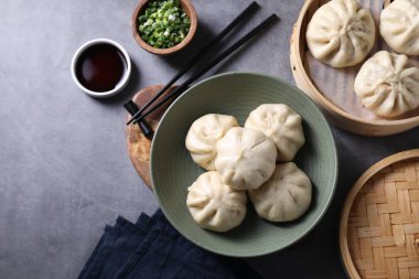 Lezzetli bao çörekleri (baozi), yemek çubukları, soya sosu ve yeşil soğan gri masada, düz uzanmış