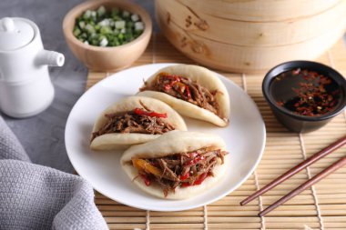 Lezzetli gua bao (domuz göbeği çörekleri), yemek çubukları, yeşil soğan ve sos gri desenli masada, yakın plan.