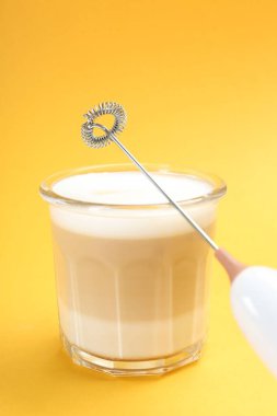 Mini mixer (milk frother) and tasty cappuccino in glass on yellow background clipart