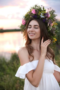 Gün batımında açık havada güzel çiçeklerden yapılmış çelenk giyen genç bir kadın.