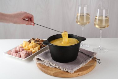 Beyaz masada erimiş peynirle fondü kabına jambon daldırmak.