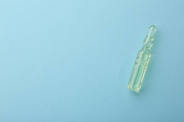 Açık mavi zemin üzerinde sıvı bulunan cam ampul, üst görüş. Metin için boşluk