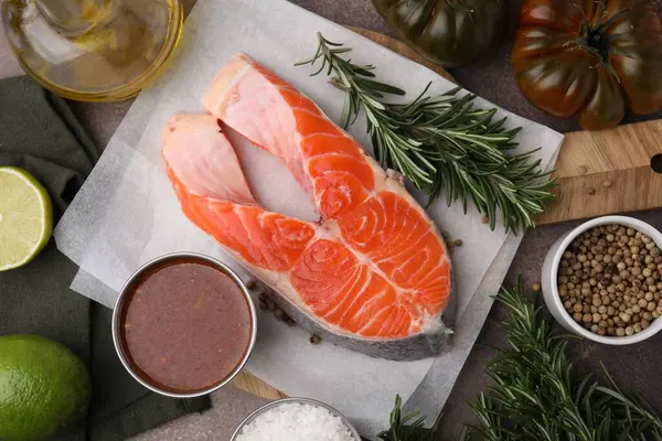 Fresh fish, products and marinade on brown table, flat lay
