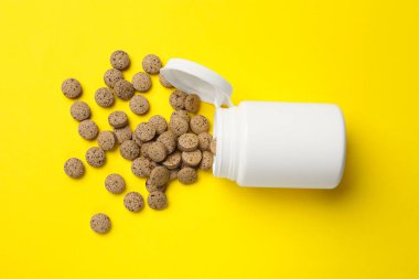 Sarı arka planda vitamin hapları ve şişe, üst manzara.