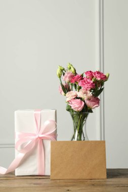 Anneler Günün kutlu olsun. Hediye kutusu, boş kart ve vazodaki güzel çiçekler beyaz duvarın yanındaki ahşap masada.