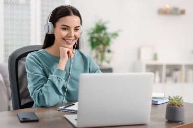 Kulaklıklı genç bir kadın masadaki Webinar 'ı izliyor.