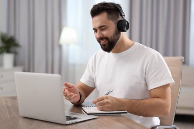Kulaklıklı genç adam masadaki Webinar sırasında görüntülü konuşma yapıyor.