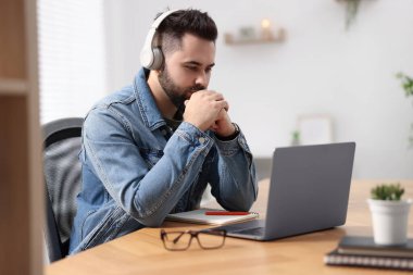 Kulaklıklı genç adam masadaki Webinar 'ı izliyor.
