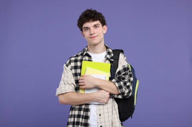 Sırt çantası ve mor arkaplan üzerine not defterleri olan öğrencinin portresi