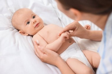 Yatakta bebeğin tenine vücut kremi süren kadın, yakın plan.