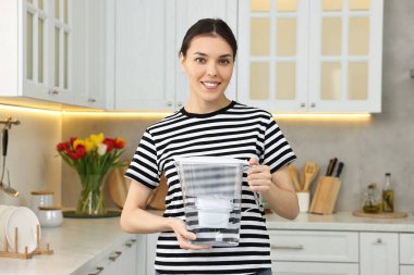 Mutfakta su dolu filtre sürahisi tutan kadın.