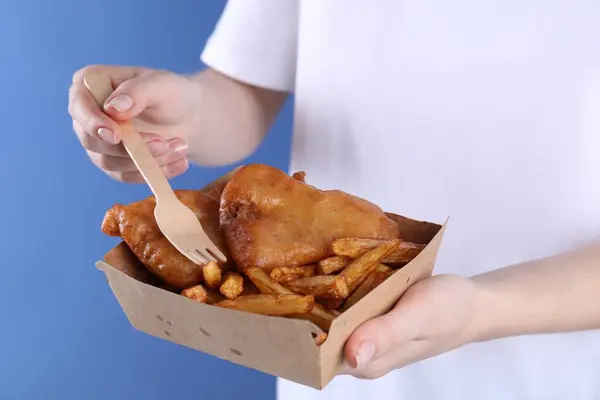 Woman eating fish and chips on blue background, closeup