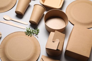 Çevre dostu gıda ambalajı. Açık gri arkaplanda kağıt kaplar, sofra takımı ve yeşil dallar