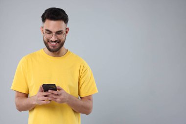 Mutlu genç adam gri arka planda akıllı telefon kullanıyor, mesaj için boşluk