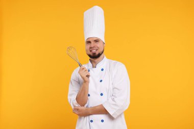 Sarı arka planda çırpı tutan üniformalı mutlu profesyonel pastacı.