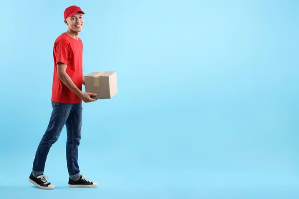 Happy courier with parcel on light blue background. Space for text