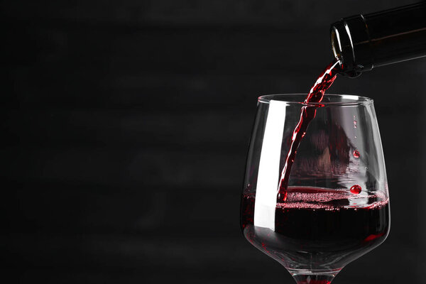 Pouring red wine into glass against dark background, closeup. Space for text
