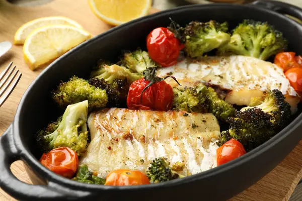 Tasty cod cooked with vegetables on wooden table, closeup