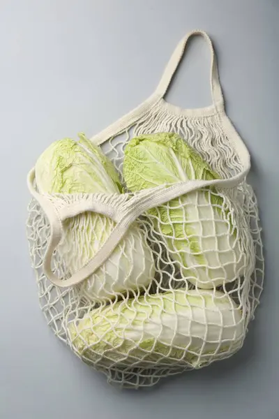 Fresh Chinese cabbages in string bag on light background, top view