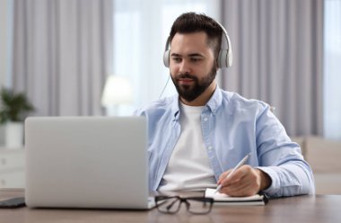 Kulaklıklı genç adam masadaki Webinar 'ı izliyor.