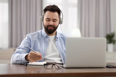 Kulaklıklı genç adam masadaki Webinar sırasında notlar yazıyor.