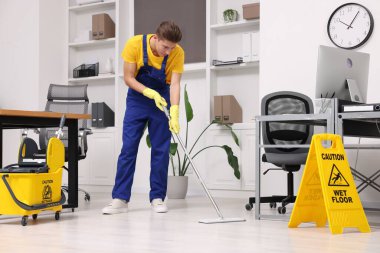 Temizlik servisi. Ofiste yerleri paspasla silen bir adam.